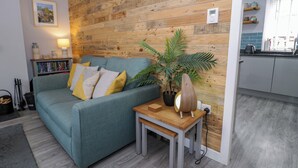 A living room with a sofa, a small table, a potted plant, and a wooden wall. - Y Bwthyn (Llanbedr)