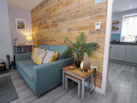 A living room with a sofa, a small table, a potted plant, and a wooden wall.