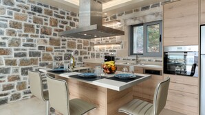 A modern kitchen with a stone wall, a central island with seating, and built-in appliances. - Unique view (Rethymno)