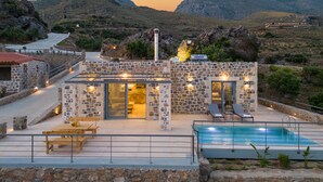 A stone building with a pool, outdoor seating, and a view of the surrounding hills. - Unique view (Rethymno)