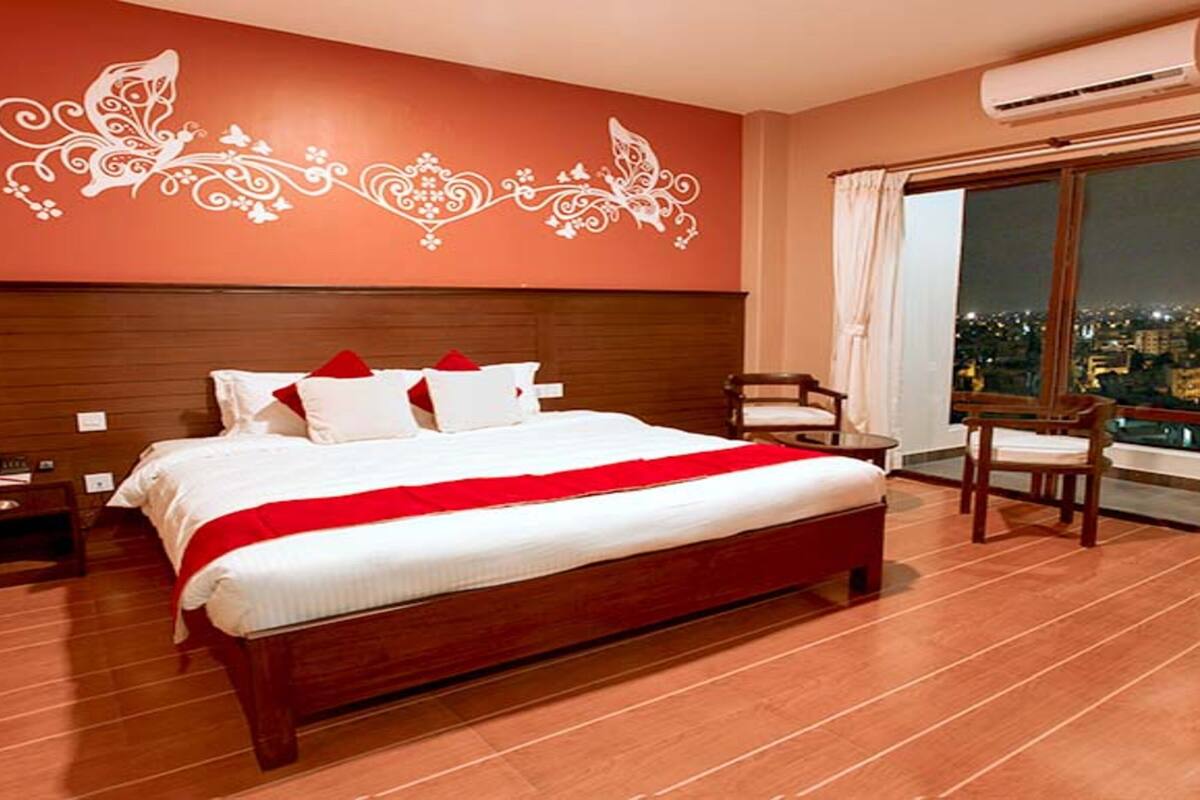 A hotel room with a large bed, a wooden headboard, a chair, a nightstand, and a window with curtains.