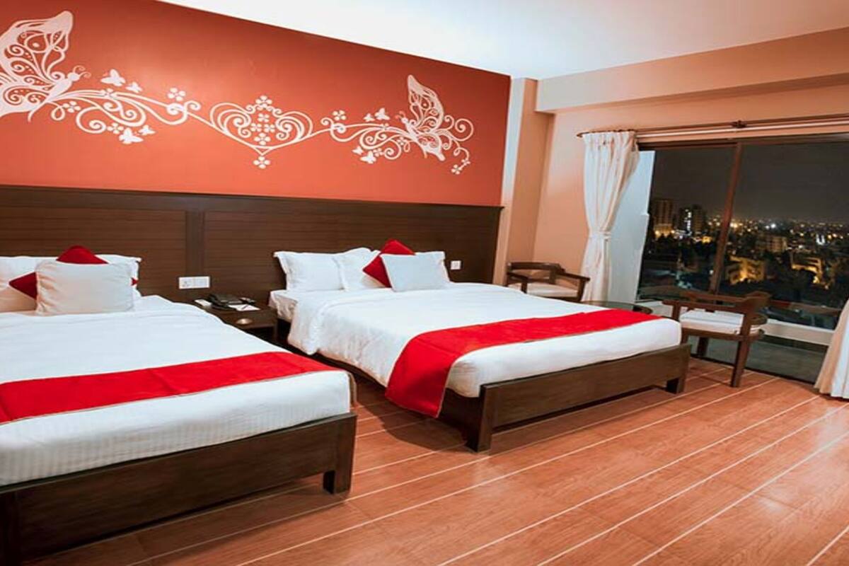 A hotel room with two beds, a large window with a city view, and a decorative wall design.