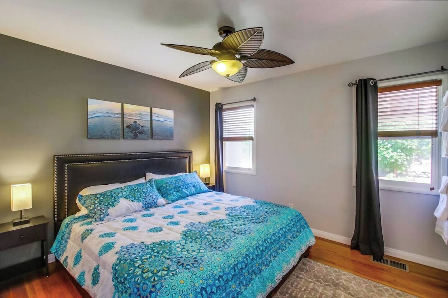 A bedroom with a bed, a ceiling fan, a window with blinds, and artwork on the wall.
