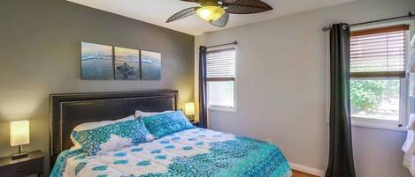 A bedroom with a bed, a ceiling fan, a window with blinds, and artwork on the wall.