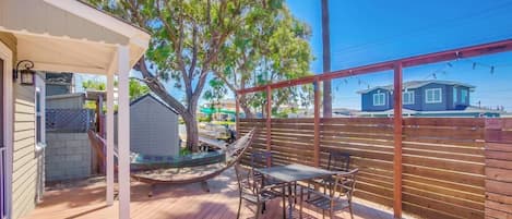 A wooden deck with a hammock, a table, and chairs, surrounded by a wooden fence and trees.