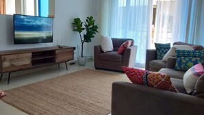 Ein modernes Wohnzimmer mit Fernseher, einer Holz-Unterhaltungseinrichtung, einer großen Pflanze und zwei Sofas mit bunten Kissen.
