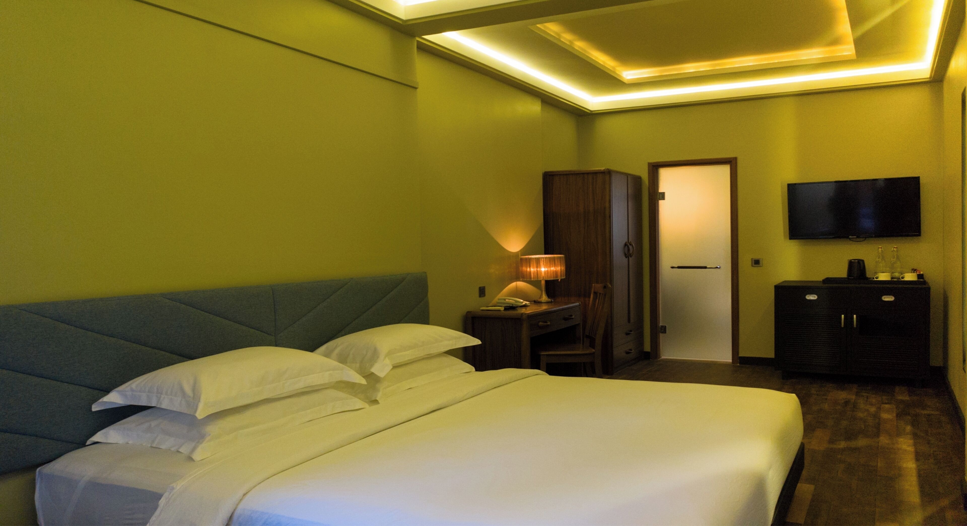 Een hotelkamer met een bed, een bureau met lamp, een televisie en een kledingkast.