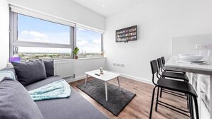 A modern apartment with a large window, a dining area, and a sofa. - Captivating 1-bed Apartment 15 min to Londonbridge (Croydon)