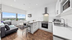 A modern kitchen with white cabinetry, a built-in oven, and a large window offering a city view. - Captivating 1-bed Apartment 15 min to Londonbridge (Croydon)