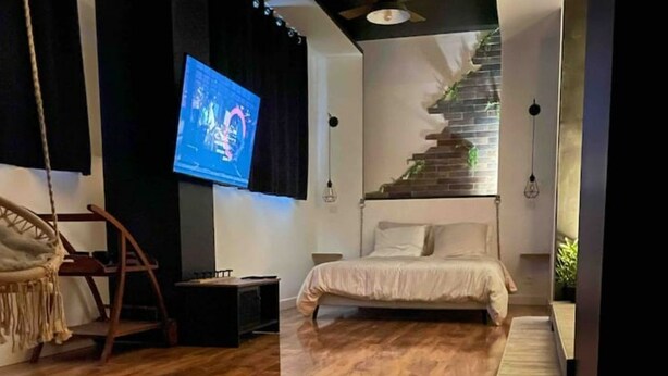 A bedroom with a wooden floor, a bed, a TV, and a staircase.