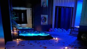 A spa area with a hot tub, wooden steps, and rose petals scattered on the floor.
