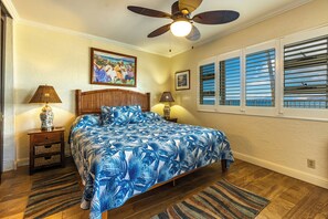 Ein Schlafzimmer mit einem Bett, zwei Nachttischen, einem Deckenventilator und einem Fenster mit Rollläden.