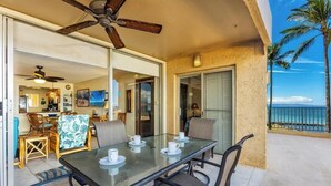 A glass-top table with chairs and a ceiling fan in a room with a view of the ocean.