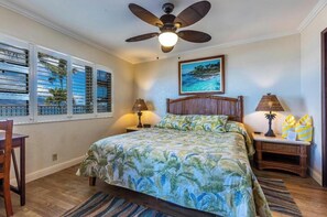 Um quarto com uma cama, um ventilador de teto, duas luminárias de cabeceira, uma janela com persianas e um quadro na parede.