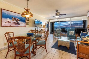 Un vaste espace de vie comprenant une table à manger, des meubles en osier et une grande fenêtre donnant sur le paysage.