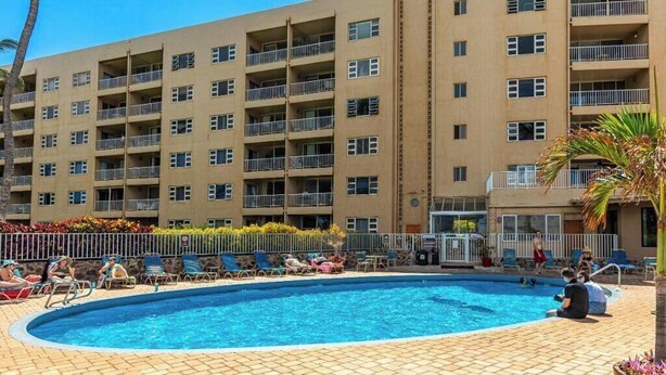 A hotel with a swimming pool, multiple balconies, and a landscaped area with lounge chairs.