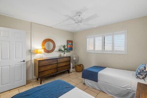 A bedroom with two beds, a ceiling fan, a dresser, a window with blinds, and a door.