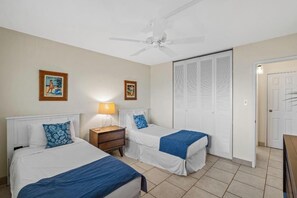 Habitación de hotel con dos camas, un ventilador de techo, una mesita de noche con lámpara y un armario con puertas batientes.