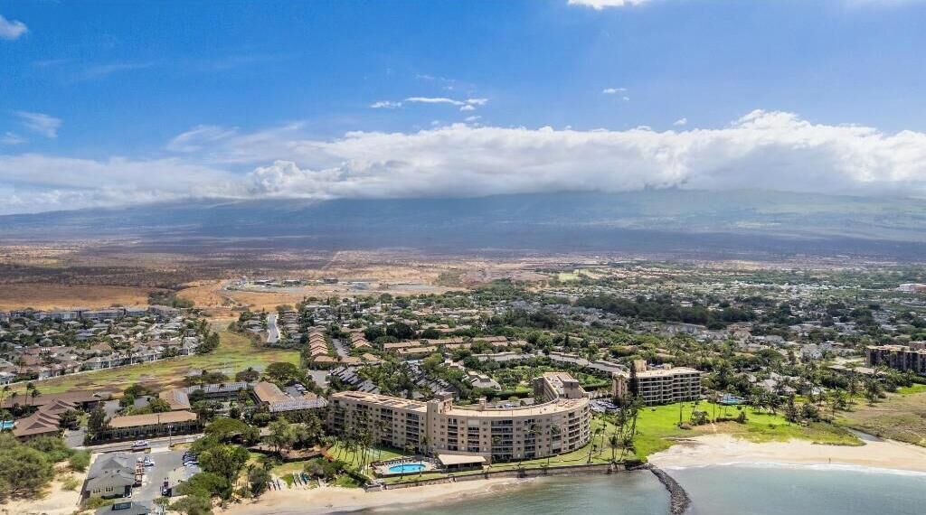 Un complex turístic costaner amb diversos edificis, una platja i vista del paisatge llunyà.