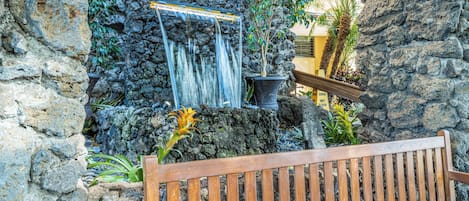 A stone wall with a waterfall feature and a wooden bench.