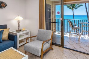 A balcony with a view of the ocean, a chair, a table, and a sofa with a lamp. - Kihei Beach Resort #504- Gorgeous Views and Coastal Elegance (Kihei, Maui)