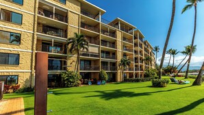 Un hotel de varios pisos con balcones, un césped cuidado y palmeras.