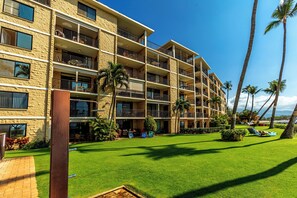 Un hotel de varios pisos con balcones, un césped cuidado y palmeras.