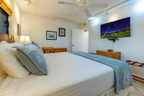 Ein ordentlich bezogenes Bett mit grauer Decke und Kissen, ein Deckenventilator, ein an der Wand befestigtes Fernsehgerät und ein gerahmtes Bild.
