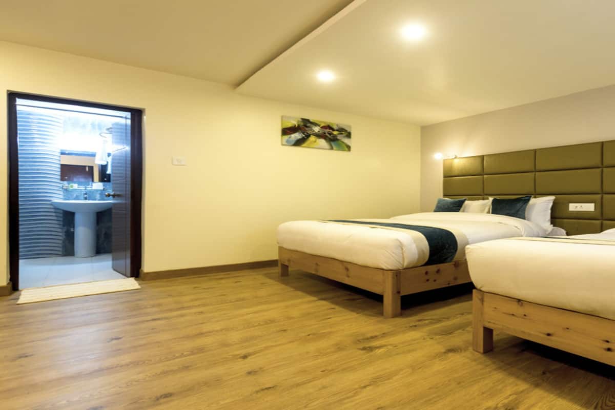 A room with two wooden beds, a wooden floor, a painting on the wall, and a bathroom visible through a glass door.