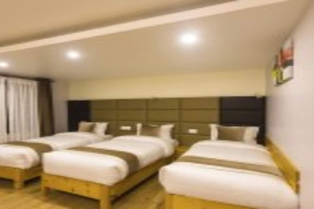 A hotel room with two single beds, a wooden headboard, and a large window with curtains.