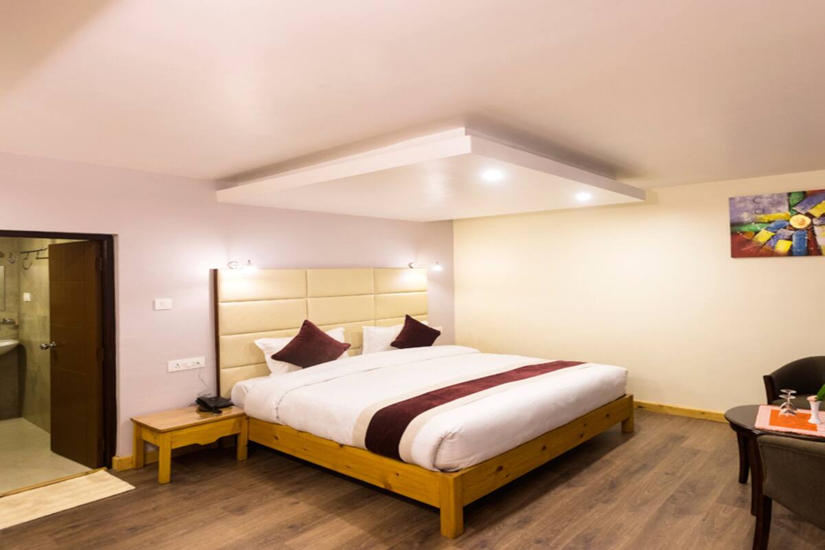 A hotel room with a wooden bed, bedside table, and a chair. There is a bathroom with a sink and mirror.