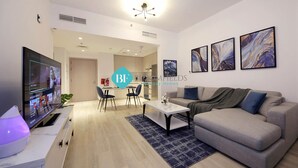 A modern living room with a sofa, coffee table, and TV. There are abstract paintings on the wall and a plant on the table. - Lavish 1BR Apartment-Yas Island (Abu Dhabi)