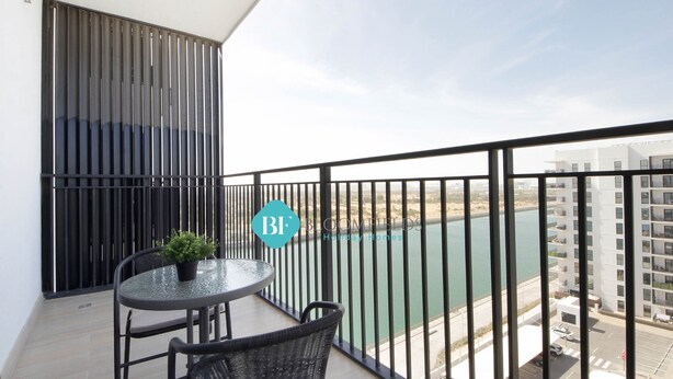 A balcony with a table and chairs, a potted plant, and a view of a body of water and buildings. - Lavish 1BR Apartment-Yas Island (Abu Dhabi)
