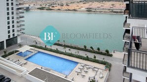 A rooftop pool area with a view of a body of water, surrounded by a modern building with balconies and a parking area. - Lavish 1BR Apartment-Yas Island (Abu Dhabi)
