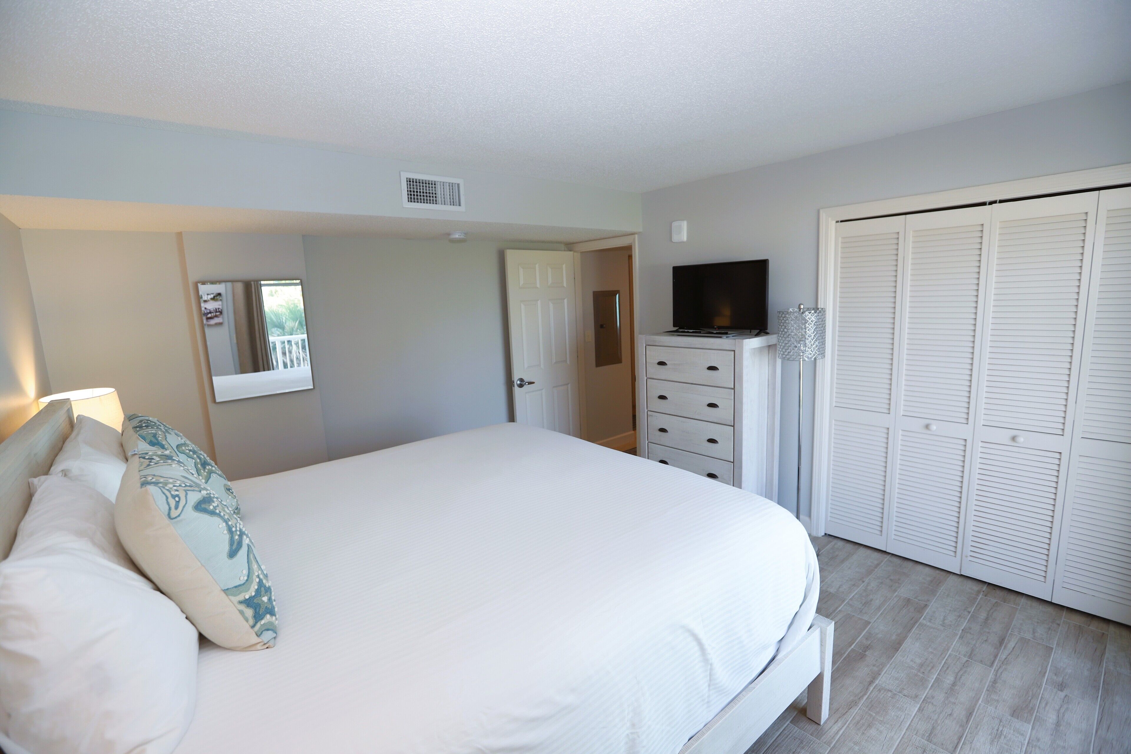 Une chambre à coucher avec un lit, une commode, un téléviseur et un placard.