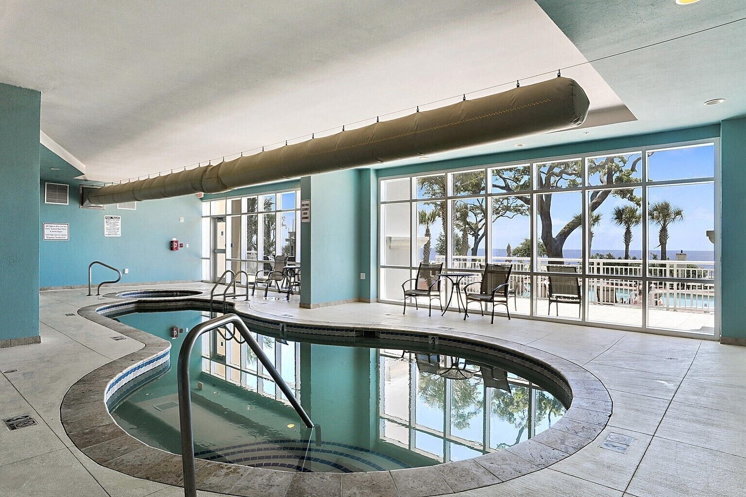 An indoor swimming pool with a view of palm trees and the ocean.
