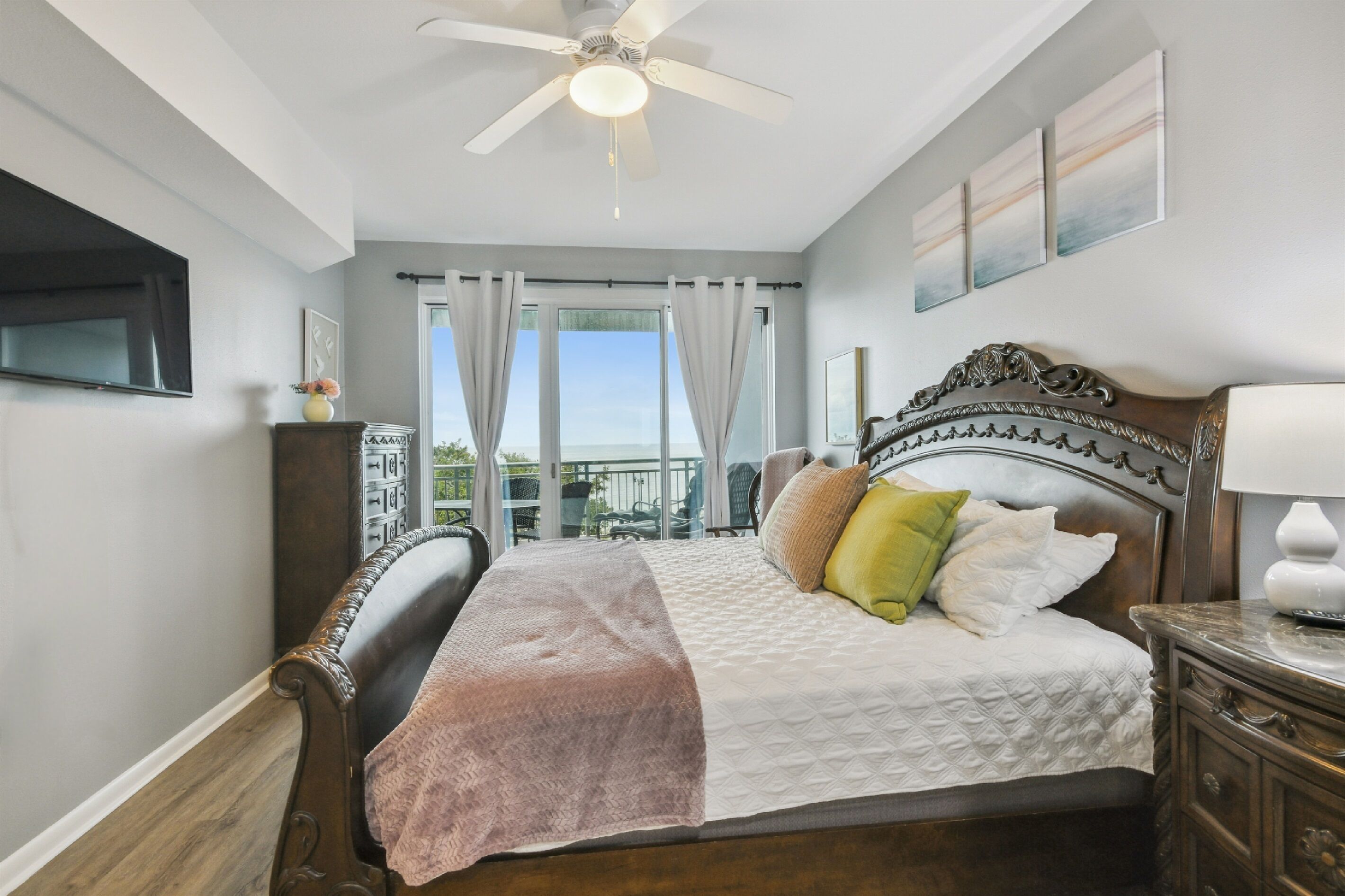 A bedroom with a bed, a ceiling fan, a TV, a nightstand, and a view of the outdoors.