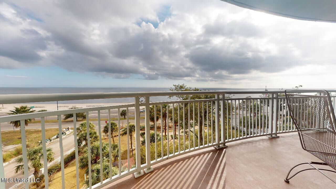 Varanda com vista para a praia e oceano, grades de metal e piso de concreto.