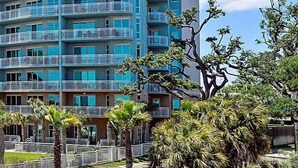 Un hotel de varios pisos con balcones, rodeado de vegetación y palmeras.