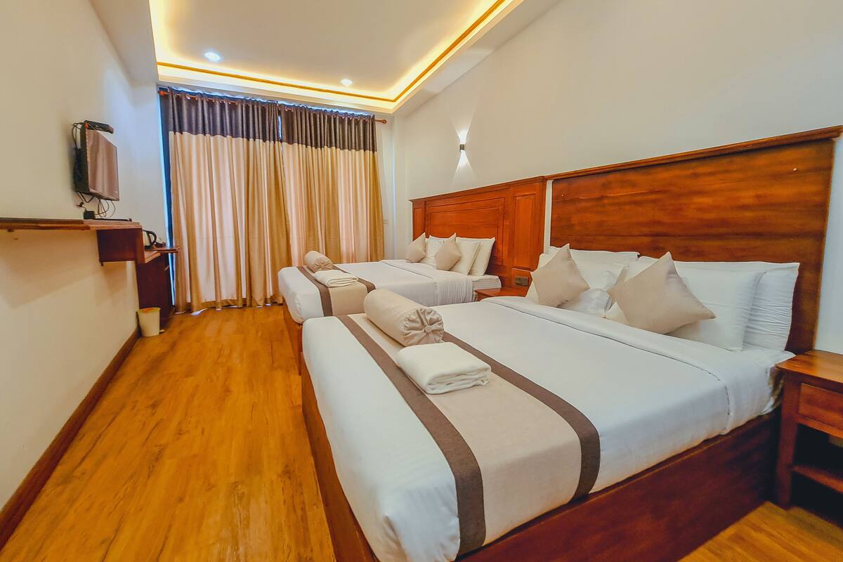 A hotel room with two beds, wooden headboards, a flat-screen TV, a wooden floor, and a large window with curtains.