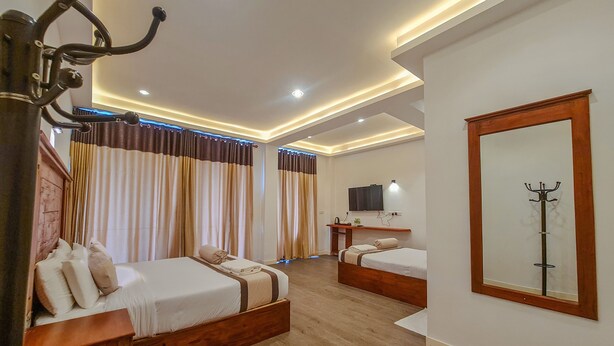 Ein Hotelzimmer mit zwei Betten, einem Holzkopfteil, einem Flachbildfernseher, einem Kleiderständer und einem Spiegel.