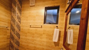 Ein Badezimmer mit Holzboden, gefliesten Duschwänden, einem Waschbecken mit Spiegel und zwei Handtüchern an Haken.
