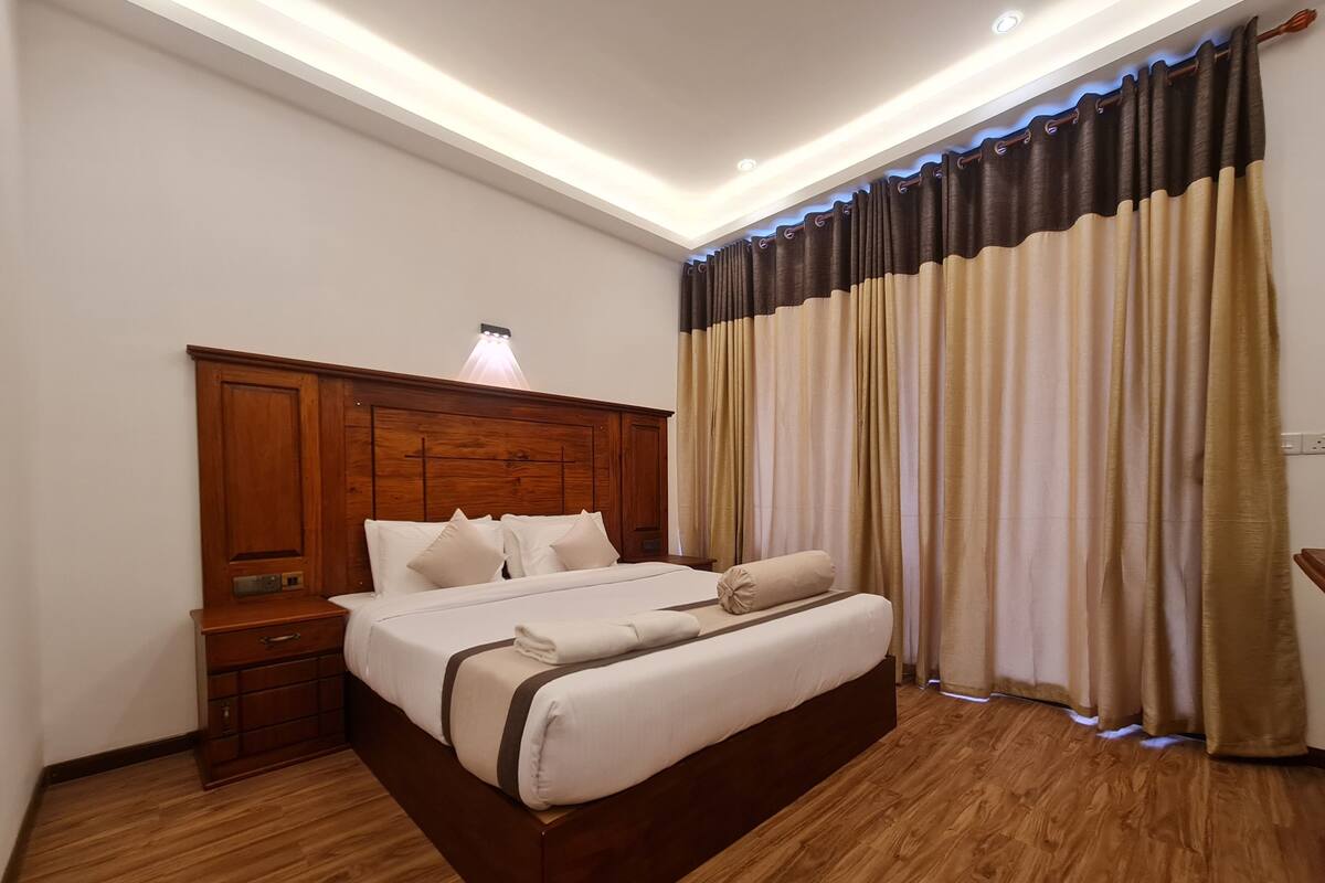 A hotel room with a wooden bed frame, a nightstand, and a large window with curtains.