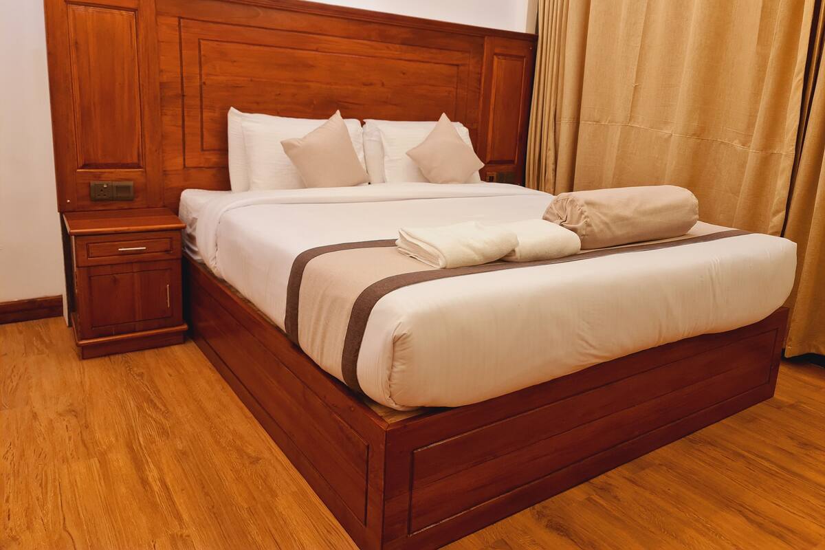 A wooden bed with a headboard, white linens, and a brown accent.