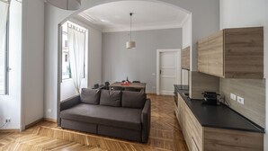 A modern living room with a grey sofa, wooden herringbone flooring, a dining area with a table and chairs, and a kitchen with wooden cabinets and a black countertop. - Lovely and new apartment near Termini Station (Roma)