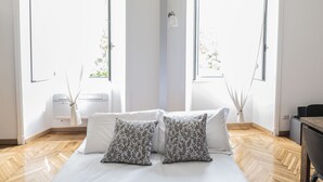 A modern bedroom with a large bed, two patterned pillows, a bedside table, and a window with a view of greenery. - Lovely and new apartment near Termini Station (Roma)