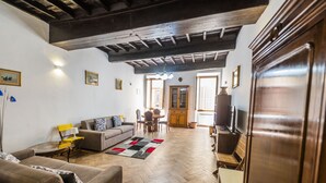 A spacious living room with a herringbone floor, wooden furniture, and a dining area with a table and chairs. - Campo de Fiori Large Family Apartment (Roma)