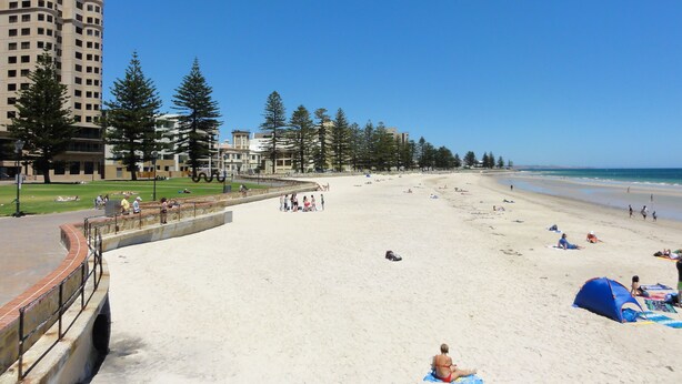 A beach with a curved walkway, beach umbrellas, and people relaxing.