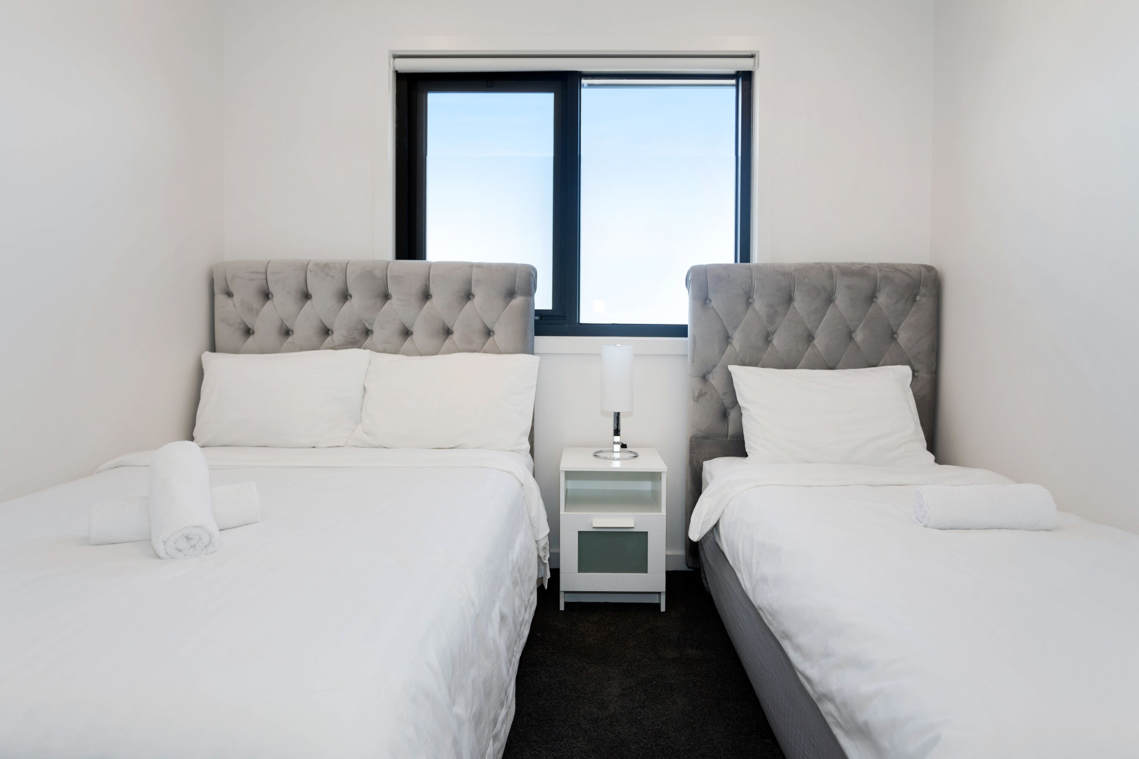 Ein Hotelzimmer mit zwei Betten, einem Nachttisch, einem Fenster und Blick zum Himmel.