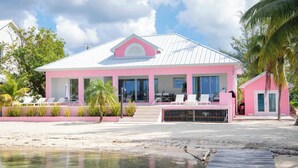 Un bâtiment rose avec un toit blanc, un quai et une plage de sable.